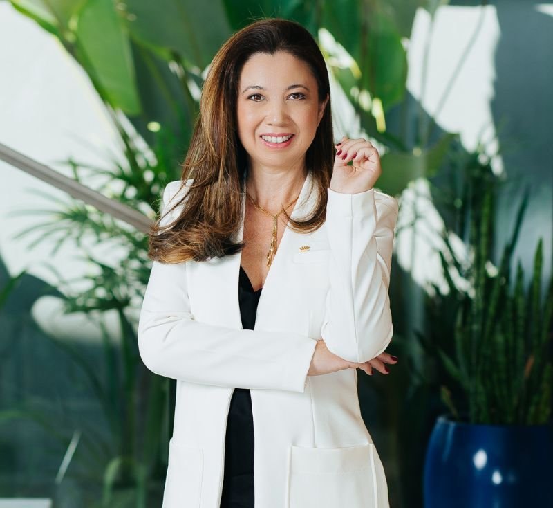 Dra. Gabriela Yano, de blazer branco, sorrindo no consultório